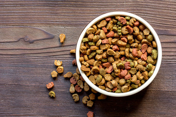 dry cat food in bowl on wooden background top view