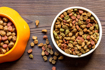 dry cat food in bowl on wooden background top view