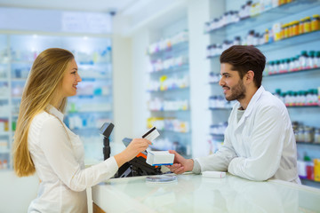 Experienced pharmacist counseling female customer in modern pharmacy, and woman pay with credit card