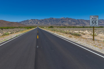 Desert highway road to horizon with a speed limit sign on a side. Nevada, USA.