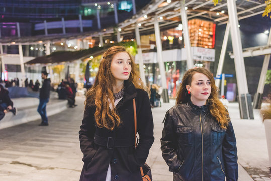 Two young beautiful caucasian women walking outdoor in the city evening, having fun interacting - friendship, interaction, having fun concept