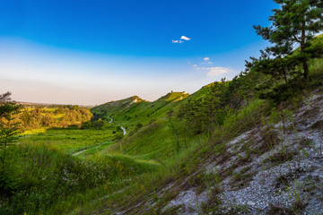 Path at the foot of ridge chalk hills. Green hills under blue sky. The archaeological monument - Krapivinskaya settlement, Belgorod region, Russia.