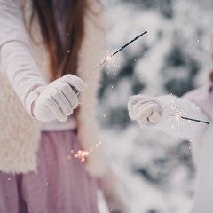 Kids playing with sparklers closeup outdoors. Wearing winter clothes and gloves over snow...