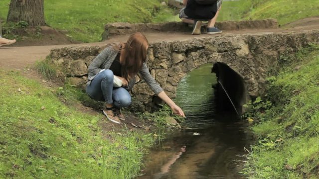The girl at the small bridge throws leaves into the stream, Peterhof, Saint Petersburg
