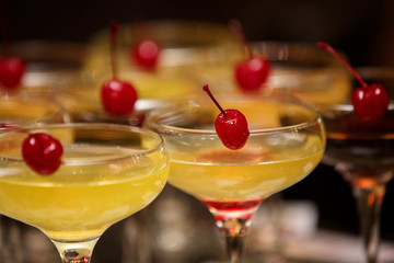 Bartender cocktails, glasses with yellow alcoholic cocktails and red cherry. 