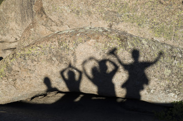 Shadows of happy people with arms raised on rock