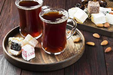 Black tea, oriental sweets, dates and nuts on a dark wooden back