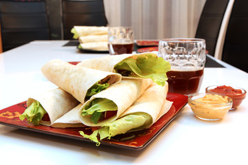 Mexican burritos on red plate, pint of beer, cheese sauce and tomato sauce 