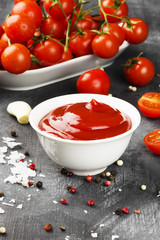 Tomato sauce in white bowl, spice and cherry tomatoes on a dark