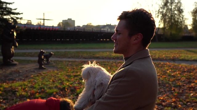 Young caucasian man hold a cute puppy. Man and pichon dog looking how lives fall. The sun shines brightly