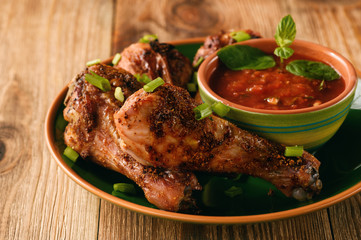 Roasted chicken legs and tomato sauce on wooden background.