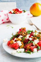Vegetarian salad with grapefruit, arugula, feta cheese, pomegranate seeds and walnuts, caramelized in honey. White plate on light table.