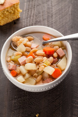 Ham and bean soup in a white bowl angled view with corn bread