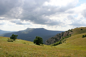 The green hillside with small trees and distant high mountain Chatyr-Dag on the summer day. This photo was taken in Crimean Mountains, on South Demerdzhi mountain. 