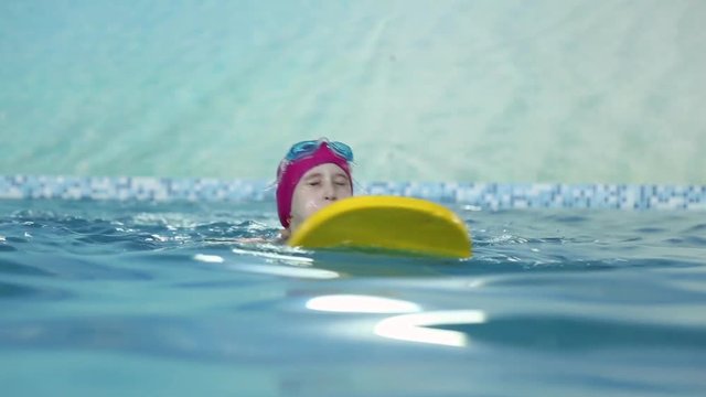 Girl learns to swim in the pool, she swims with a foam plastic board
