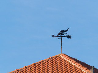 weather vane shaped like tree dolphins placed on top of a roof made of terracotta tiles
