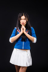 Attentive Asian woman clasped her hands and looking away while expressing positive and negative emotions isolated on black background in studio.