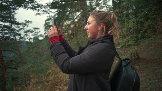A young woman taking a photo in a beautiful forest with a smartphone slow motion
