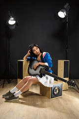 Fototapeta premium Beautiful Asian rock star lady sitting and holding guitar in studio. Pretty brunette lady resting after hard rock music.