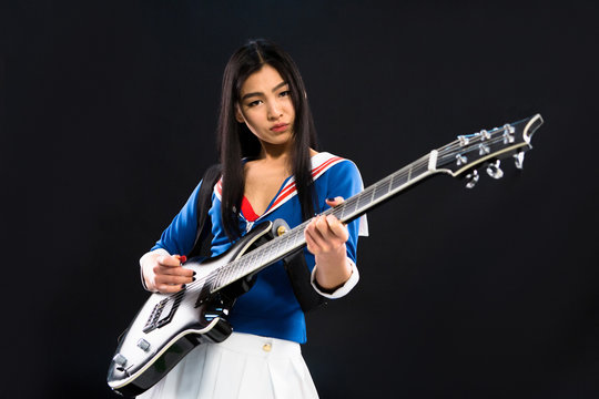 Asian rock star lady playing hard rock on guitar while posing for photographer isolated on black background in studio.
