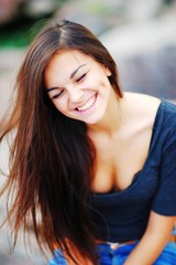 Young beautiful long-haired girl genuinely laugh, eyes closed, outdoors, close-up.