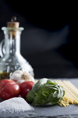 ingredients for a pasta with spaghetti, tomato, basil and extra virgin olive oil on black plate