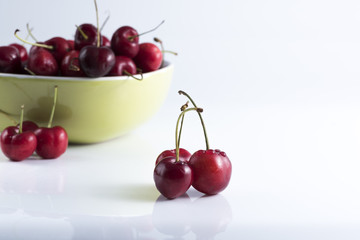 red cherries laid on a clear foreground and background cherries in a bowl.