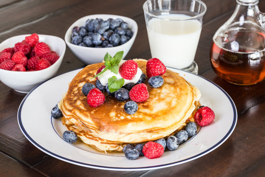 pancakes with fresh berries, milk and maple syrup/Pile of pancakes with blueberries and raspberries with maple syrup on the white plate