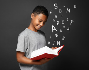 African-American boy with book and alphabet letters on dark background. Speech therapy concept