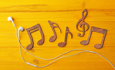 Musical notes and earphones on yellow wooden background