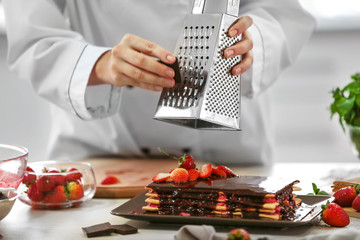Cooking concept. Professional confectioner decorating delicious cake with grating chocolate, closeup