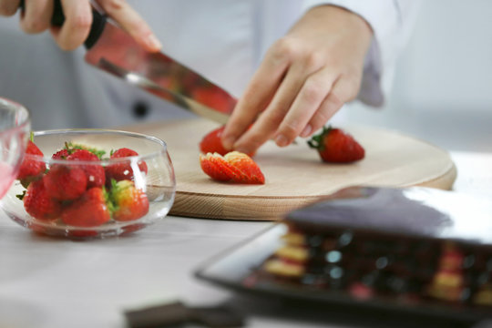 Cooking concept. Professional confectioner chopping strawberry on cutting board, closeup