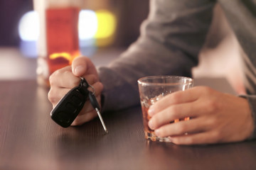 Man sitting in bar with car key and glass of alcoholic beverage, closeup. Don't drink and drive concept