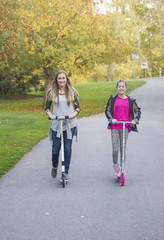 A happy girl and her mother riding together outdoors on a paved bike pathway. Smiling and having fun together at an outdoor city park