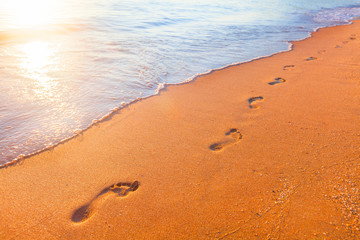 beach, wave and footprints at sunset time