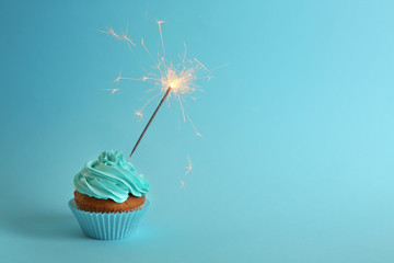 Fresh tasty cupcake with sparkler on blue background - Powered by Adobe