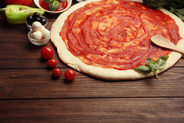 Raw pizza dough with sauce and ingredients on wooden table