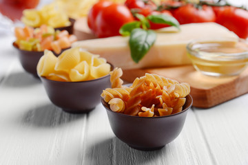 Different kinds of pasta and tomatoes on wooden background