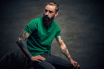 Tattooed bearded male sits on a chair.