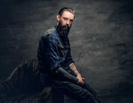 Tattooed bearded male sits on a chair.