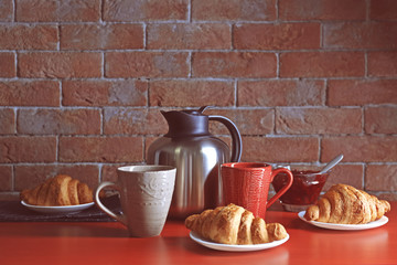 Thermos kettle with cups and croissants on red table