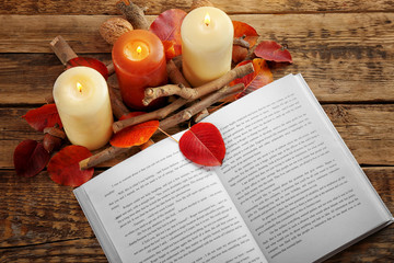 Fototapeta na wymiar Beautiful composition of book, autumn leaves and alight candles on wooden background