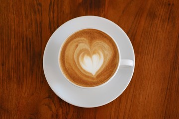 Hot coffee with heart make up on face of milk cream in white cup on wooden table background.