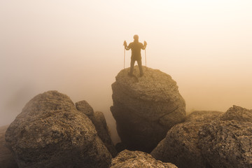 Man hiking to the top of the mountain, shrouded in fog during ye