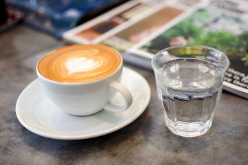 Hot coffee with heart make up on face of milk cream in white cup and water in glasses on vintage table background.