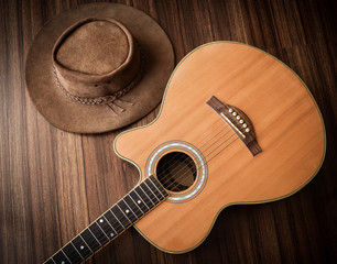 Acoustic guitar and leather cowboy hat laid on wooden floor background,low key.
