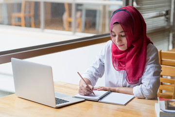 Muslim woman working with computer and writing notebook.