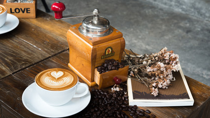 A Coffee Bean Grinder with Spilled Coffee Beans with a Cup of Coffee, Flowers and a Book