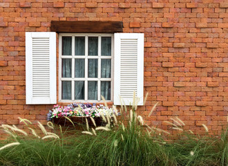 Flowers with green grass and white wooden window on brick wall