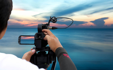 Obraz premium Man recording a sunset on the ocean with video recorder